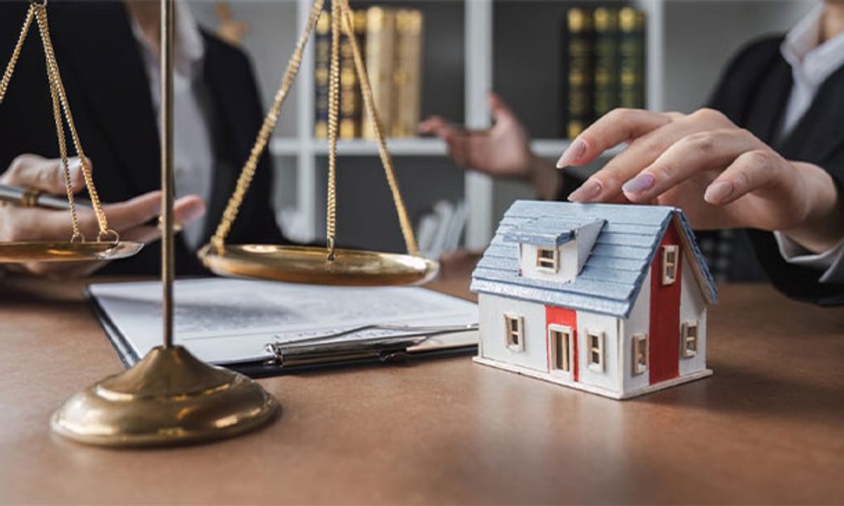 Scales of justice beside a model house on an attorney’s desk